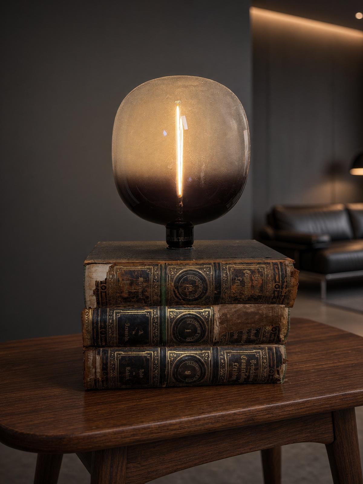 Tischleuchte mit Rauchglas-Lampe auf einem Stapel antiker Bücher